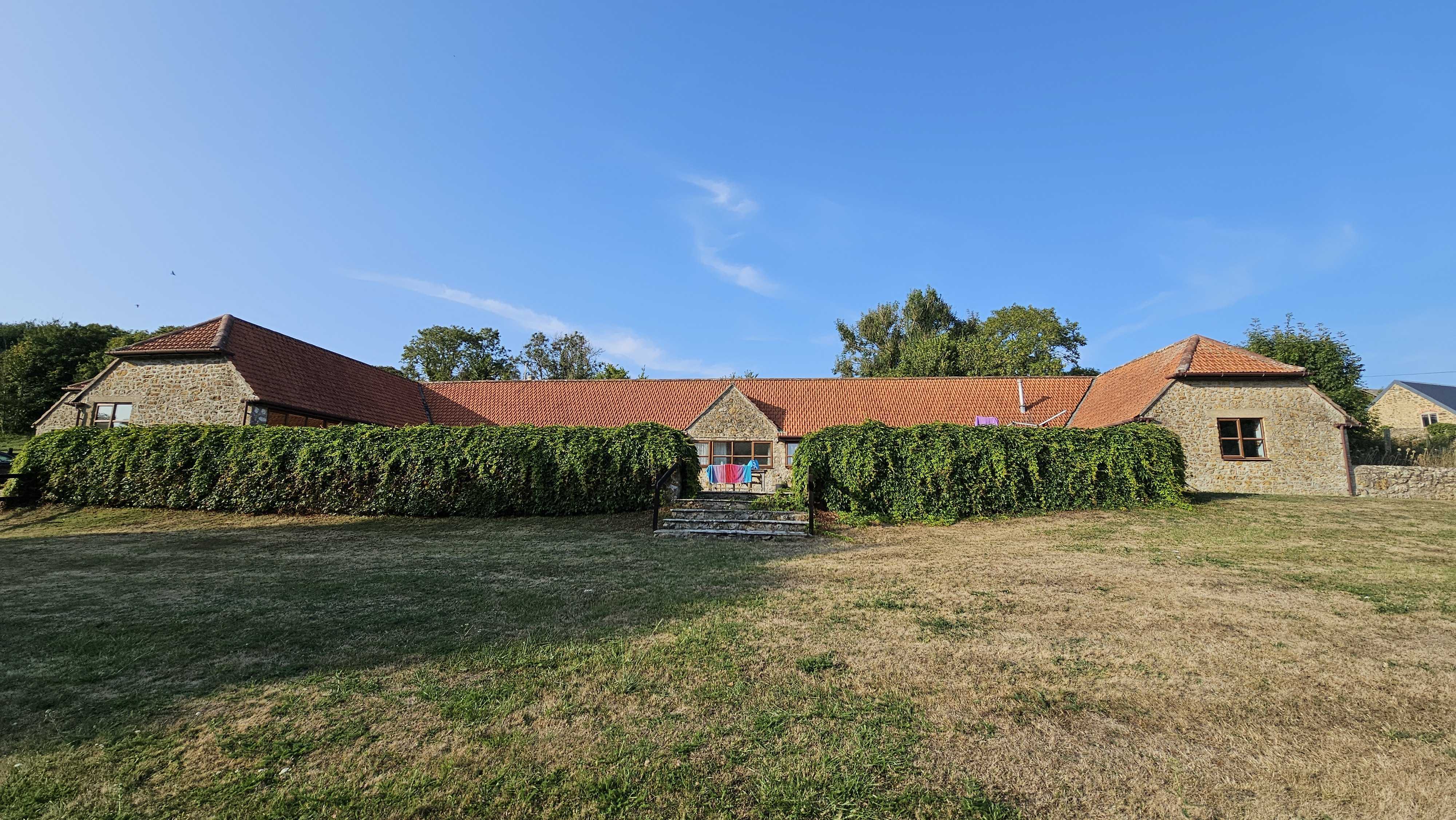 The Old Piggeries - view across the rear lawn showing the cottage behind a tall beech hedge.